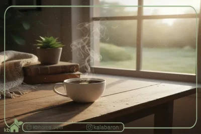 فنجان قهوه بخارآلود روی میز چوبی کنار پنجره با نور صبح